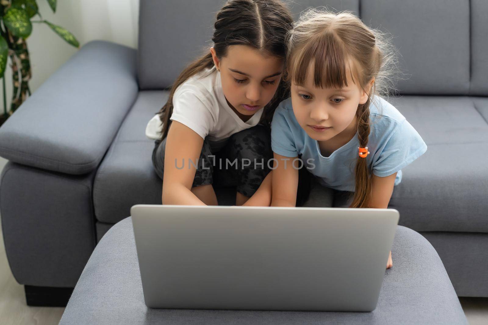 Two girls working on laptop, smiling and older sister help younger.