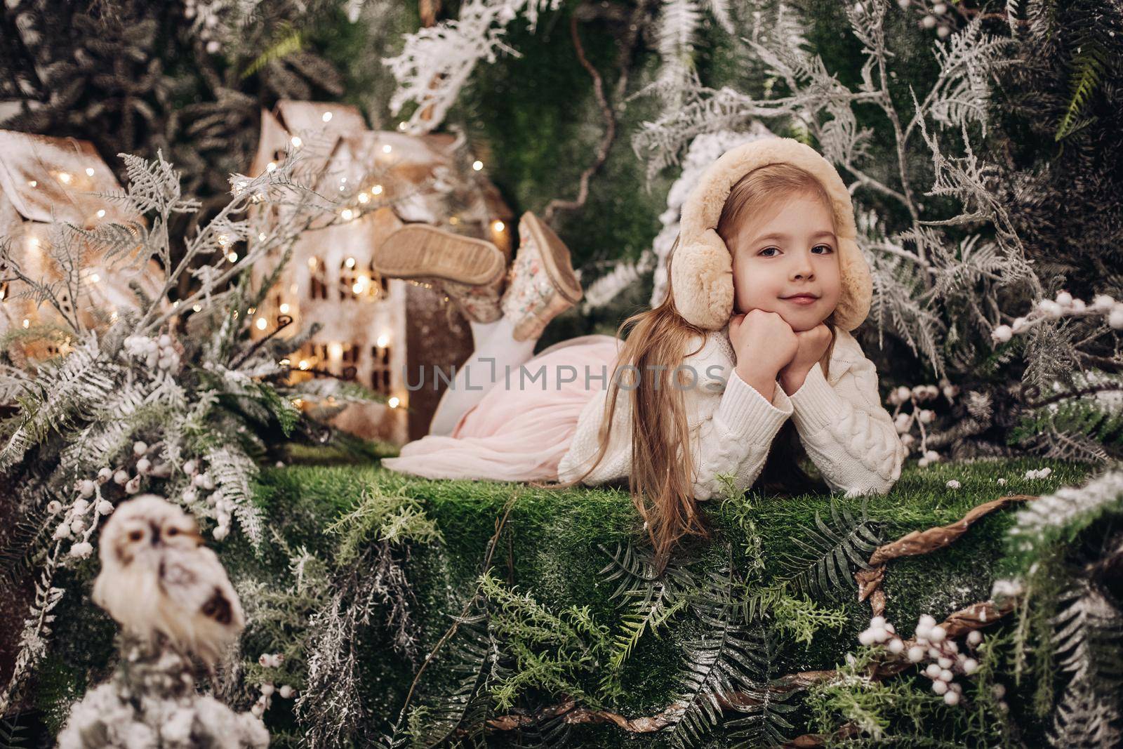 handsome caucasian child with long fair hair lies in christmas atmosphere with a lot of decorate trees around her