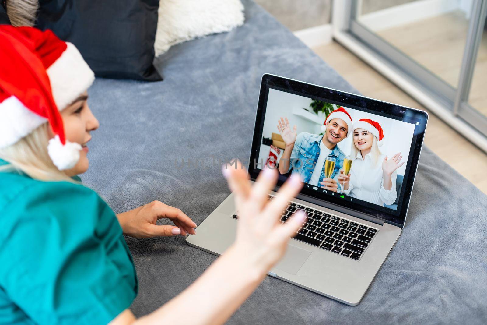 Smiling girl wearing Santa hat having video calling family by webcam. Woman with laptop sitting on kitchen at home using virtual meeting chat on holidays. Happy Christmas and New Year new normal. by Andelov13