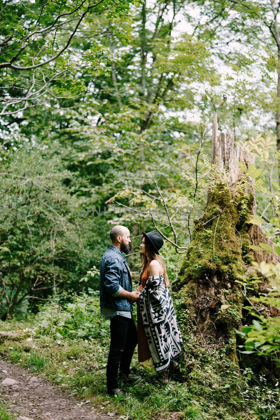 Man and pregnant woman stand near mossy tree near path in park. High quality photo