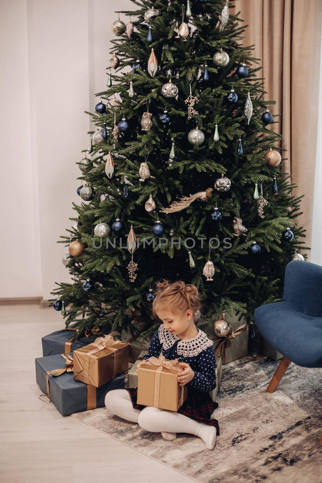 little caucasian girl looks her girt near the christmas tree at home by StudioLucky