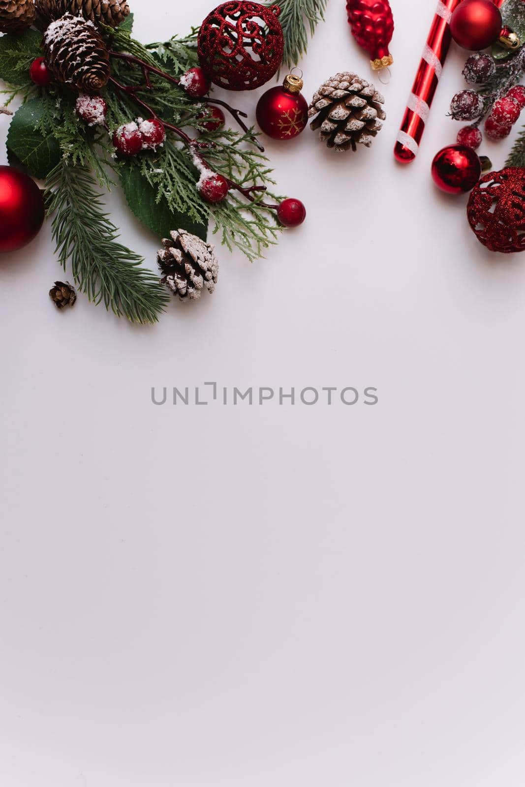 Fir branch with Christmas red decorations and balls on a white background with copy space for text. Vertical photo.