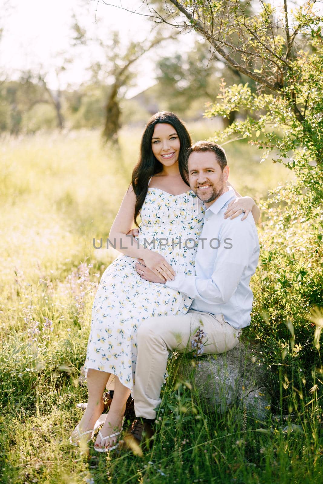 Pregnant woman sits in the arms of a man sitting on a stone by Nadtochiy