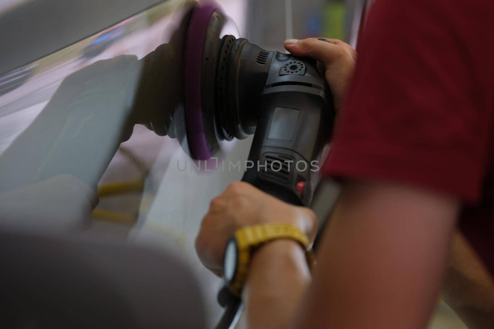 A repairman polishes a car body, close-up of a hand. Equipment for removing scratches, removing paint irregularities