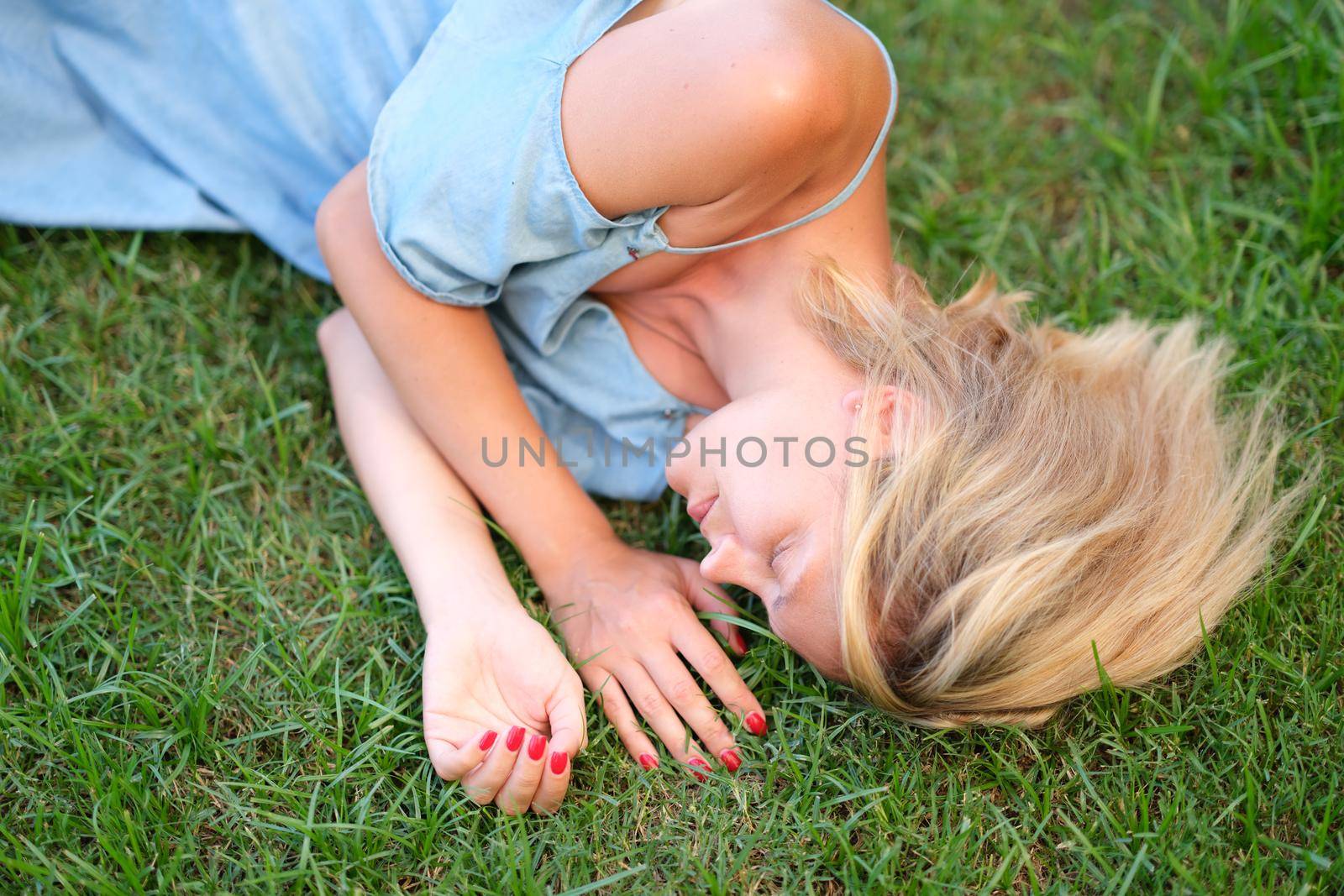 A young woman in a dress is sleeping on the green grass, close-up. Unity with nature, healthy ecology, relaxation