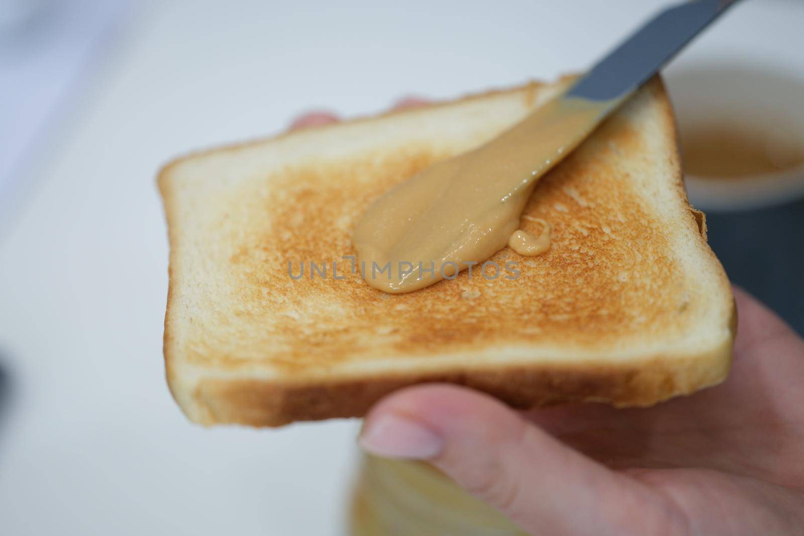 In hands toasted toast with peanut butter, close-up. Spread the nut butter with a knife, breakfast. Snack at home