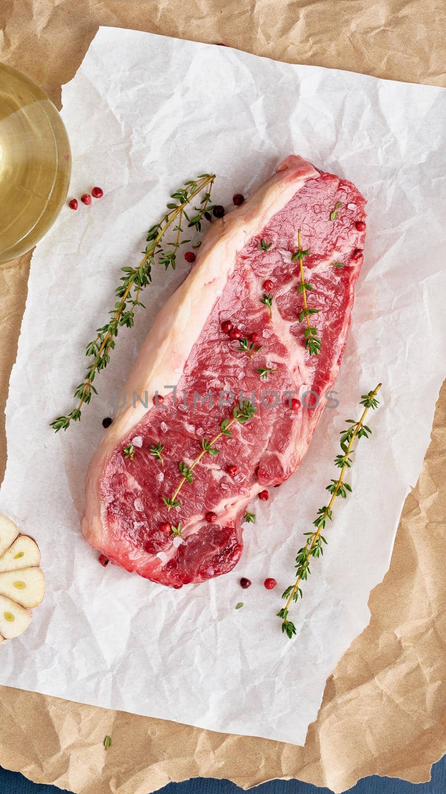 Big whole piece of raw beef meat, striploin on white parchment paper on craft background, zero waste packing. Seasoning steak with salt, vertical