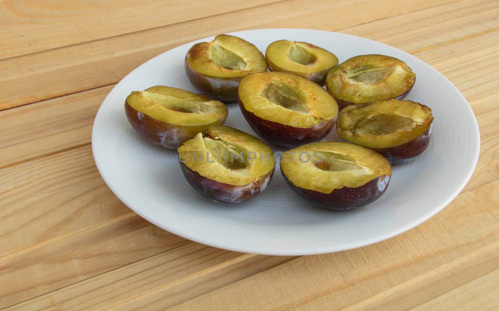 Sliced tasty juicy plums on a plate, wooden background.