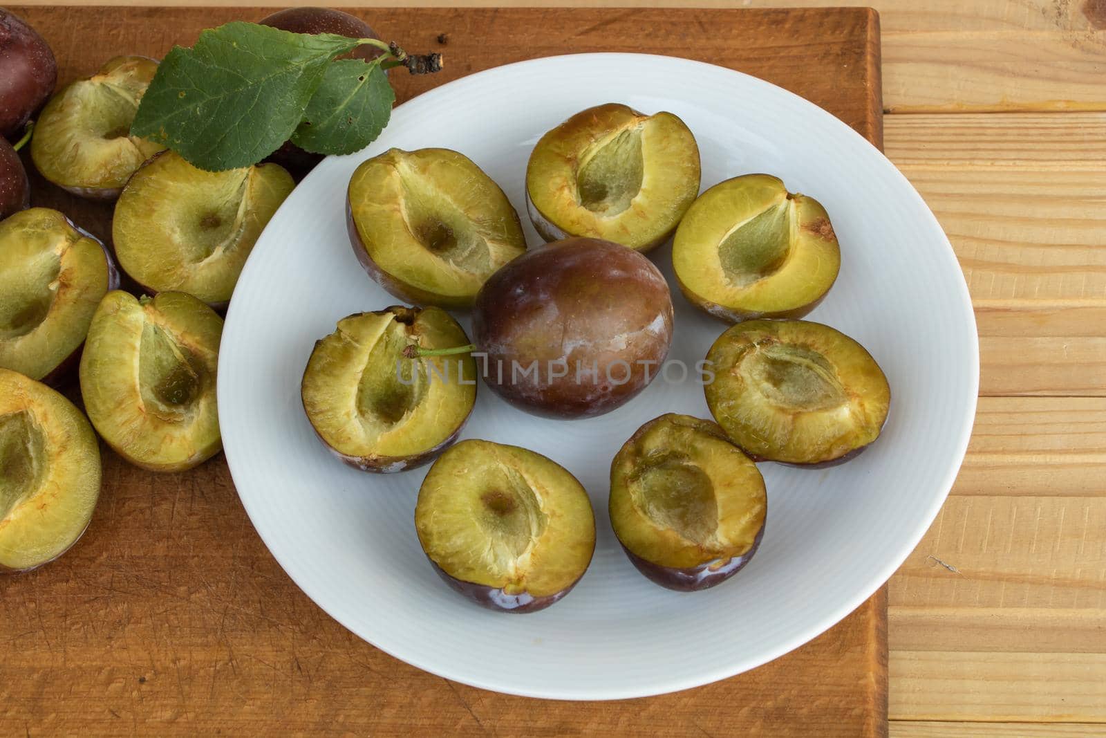 Sliced tasty juicy plums on a plate, wooden background.