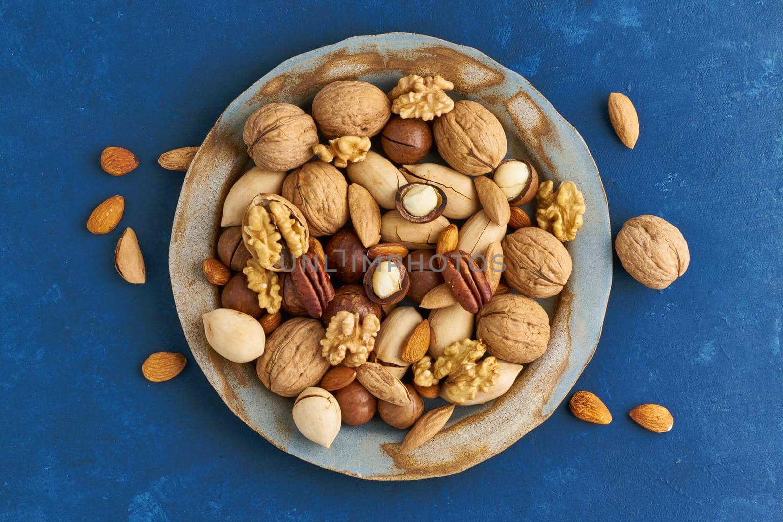 Classic blue in a food. Mix of nuts on plate - walnut, almonds, pecans, macadamia and knife for opening shell. Healthy vegan food. Clean eating, balanced diet. Top view