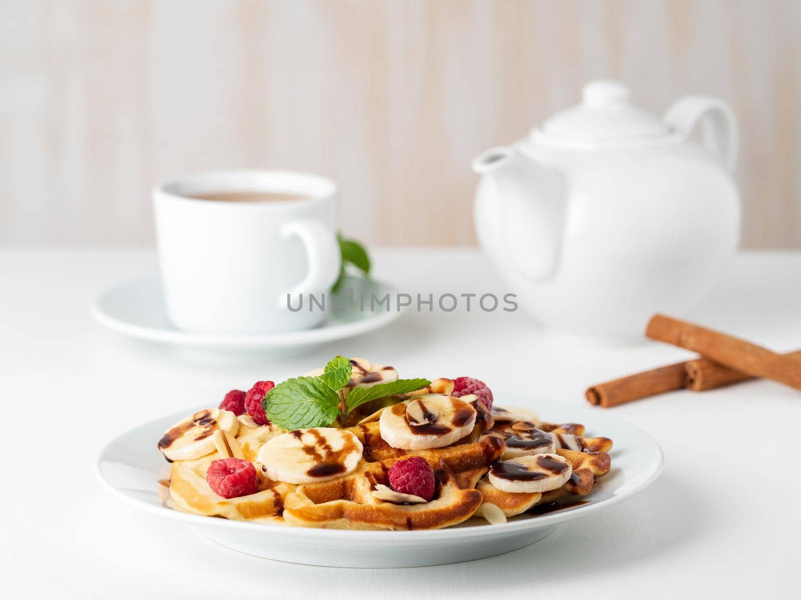 Belgian curd waffles with raspberries, banana, chocolate syrup. Breakfast with tea on white background, side view