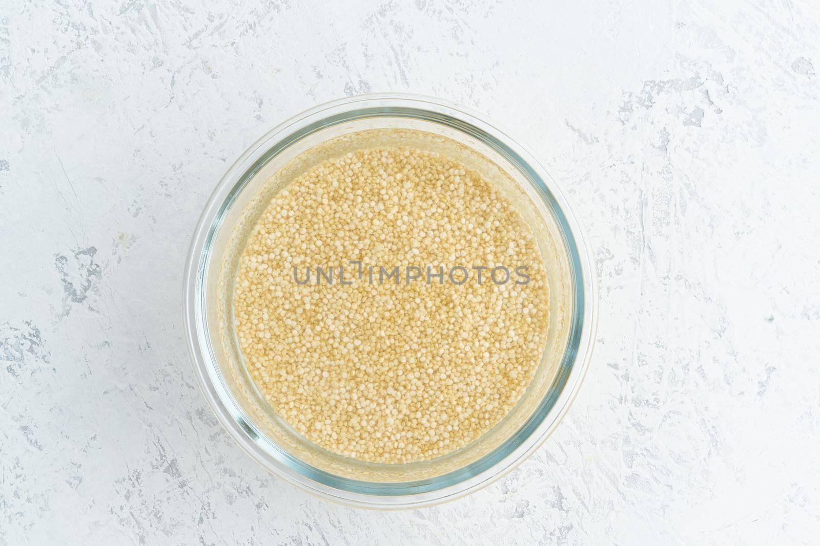 Soaking quinoa cereal in a water to ferment cereals and neutralize phytic acid. Large glass bowl with grains flooded with water. Top view, close up, white background