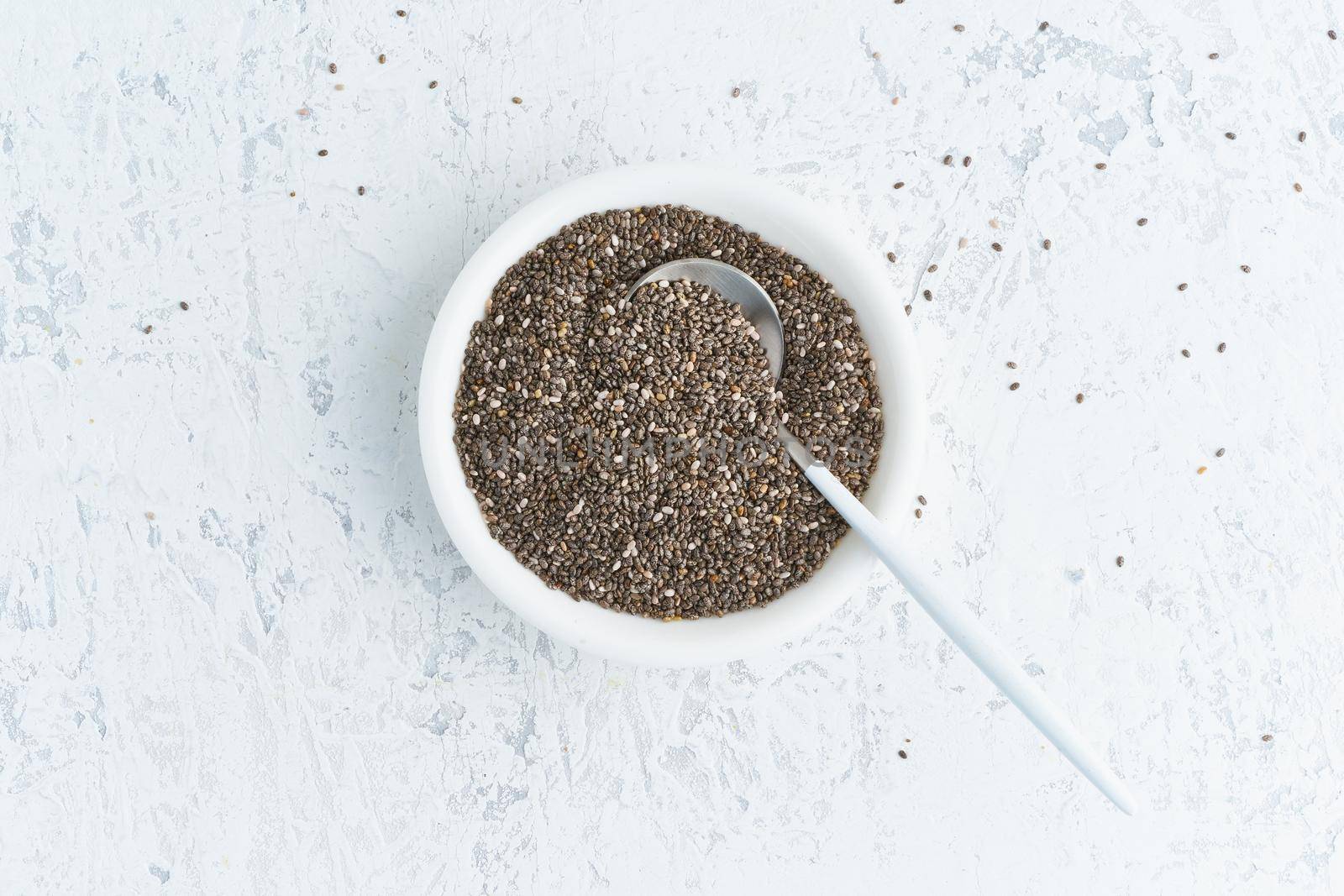 Chia seeds in white bowl on a white stone concrete background, top view, copy space