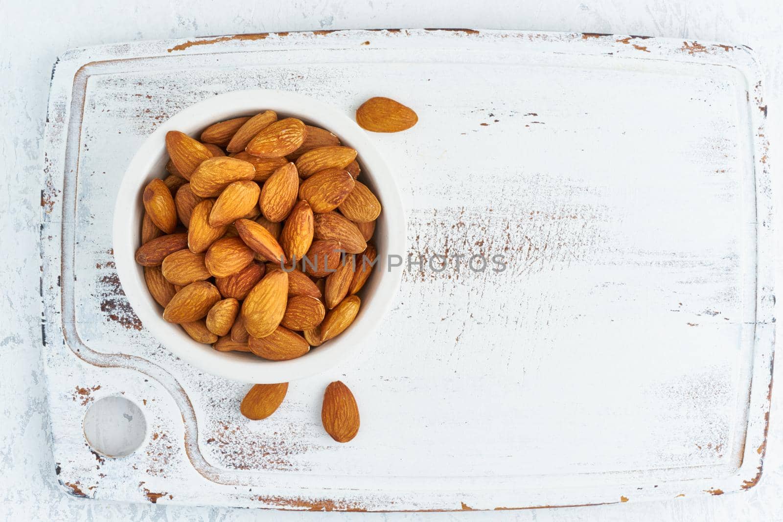 Top view almonds nuts in a white bowl on a white wooden cutting board. Wooden background, overhead, copy space, close up