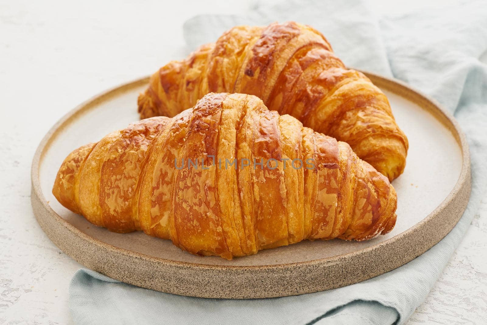 Two delicious croissants on a plate and a hot drink in a mug. Morning French breakfast with fresh pastries. Light gray background.