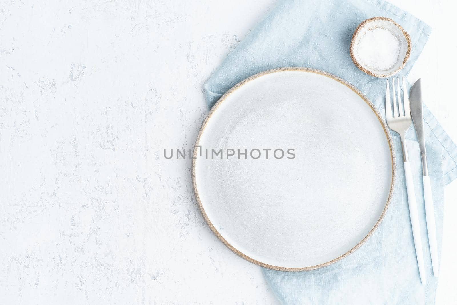 Clean empty white ceramic plate, fork and knife on white stone table, copy space, mock up, top view. Concept for menu with utensil