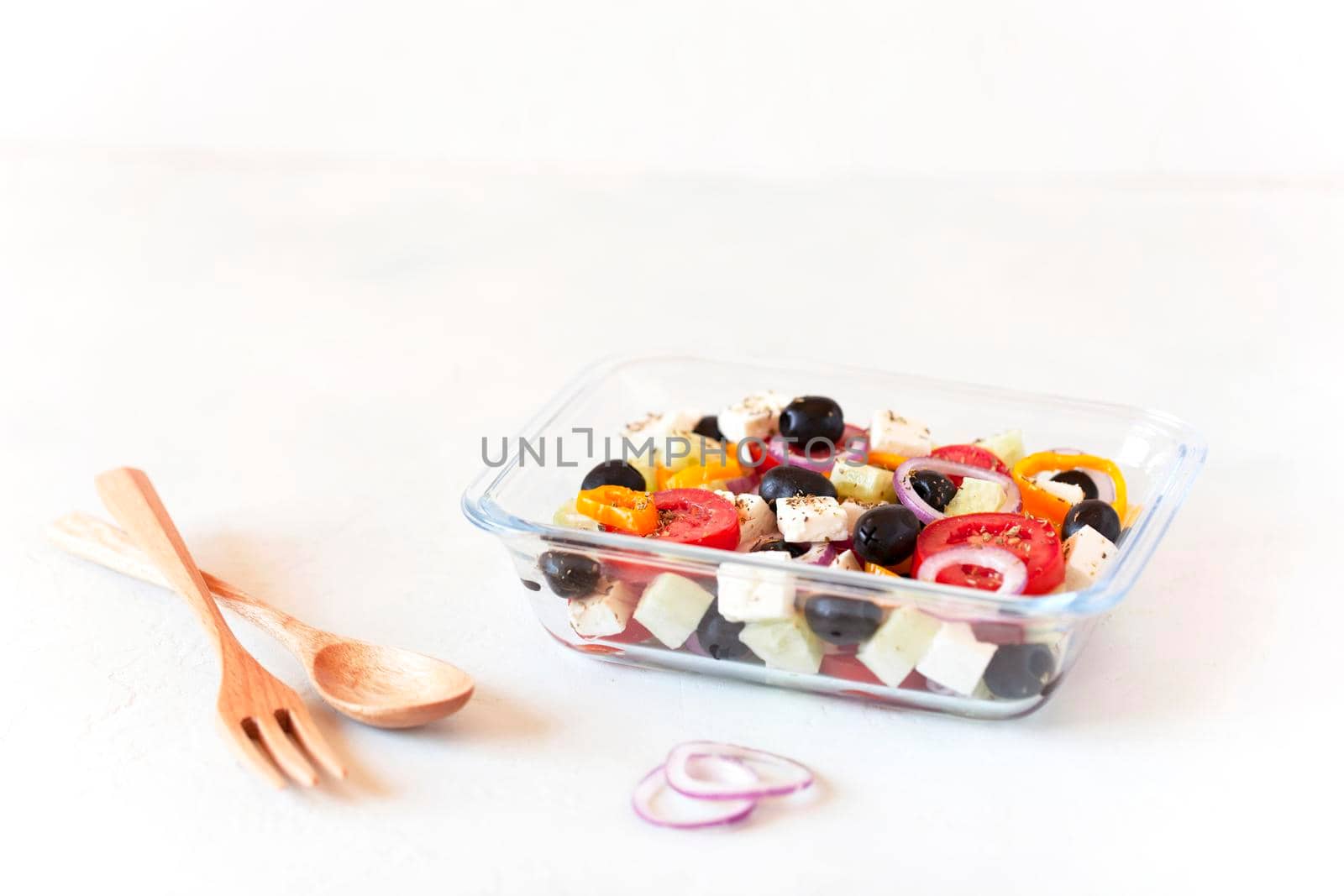 lunch box with greek salad, reusable glass container, wooden cutlery, on white background, side view