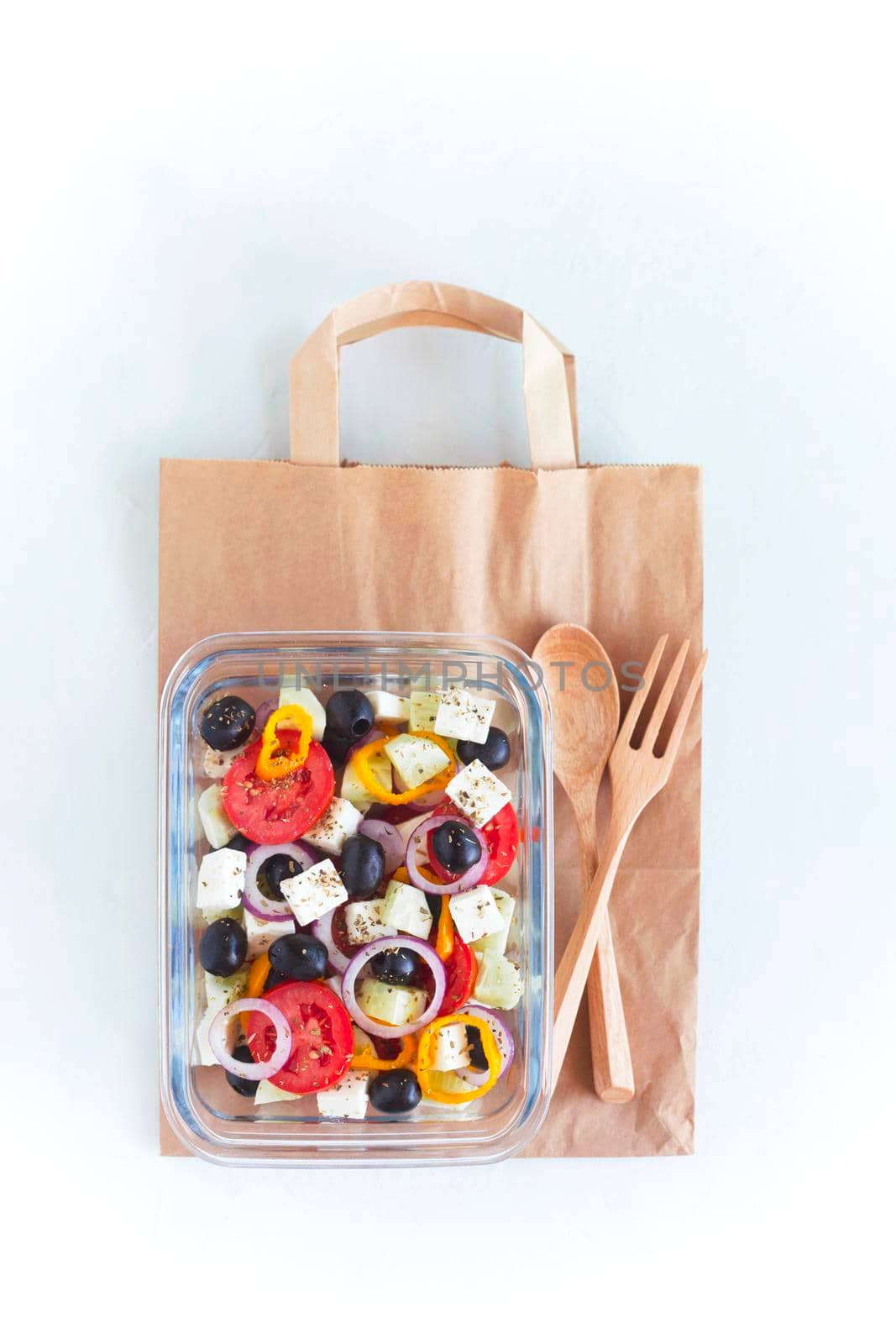 lunch box with greek salad on the paper bag with wooden fork and spoon, on white background, concept of healthy food and zero waste, top view