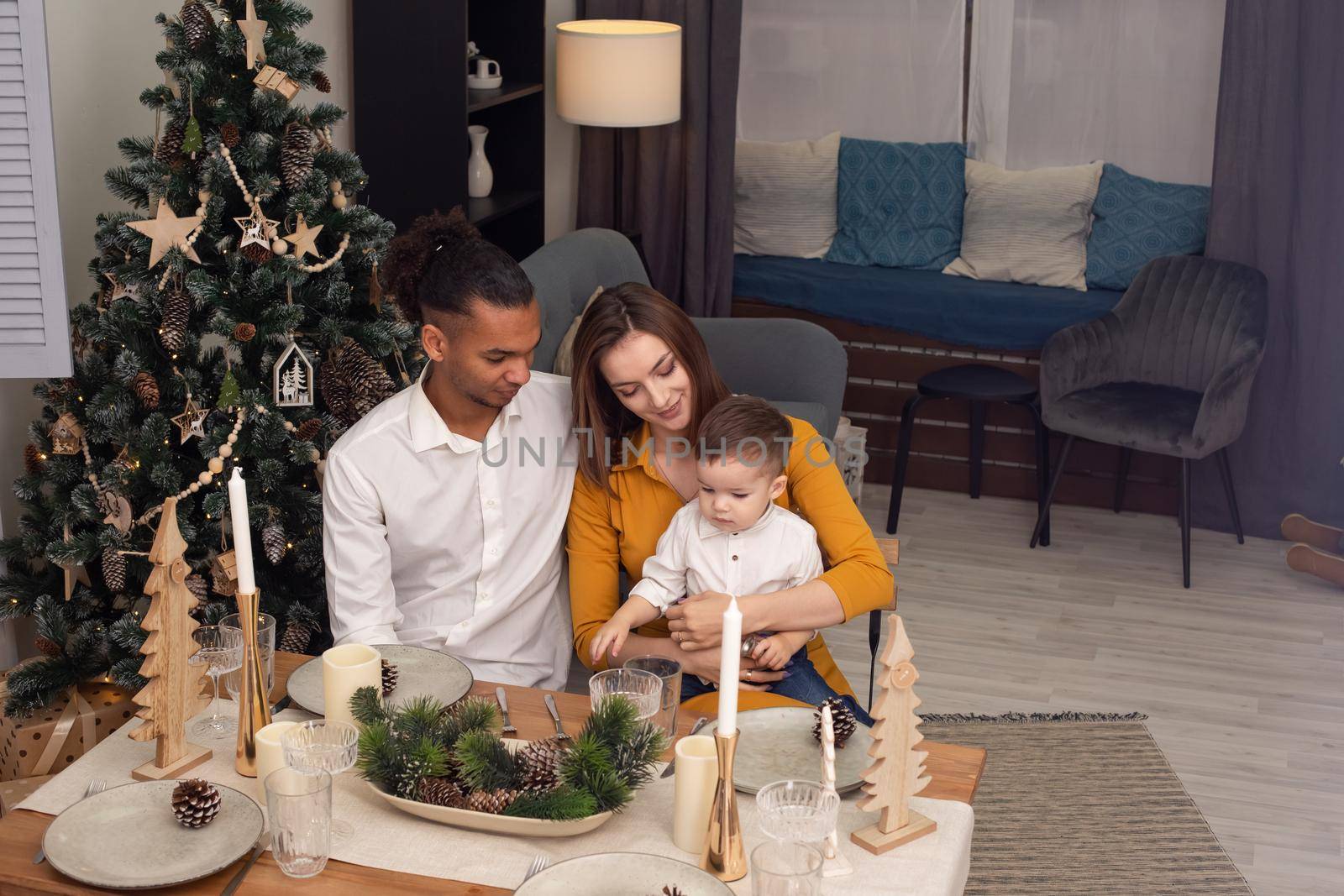 A young multiracial sitting at a wooden table with serving in an eco style, in a living room decorated for Christmas. by Zakharova