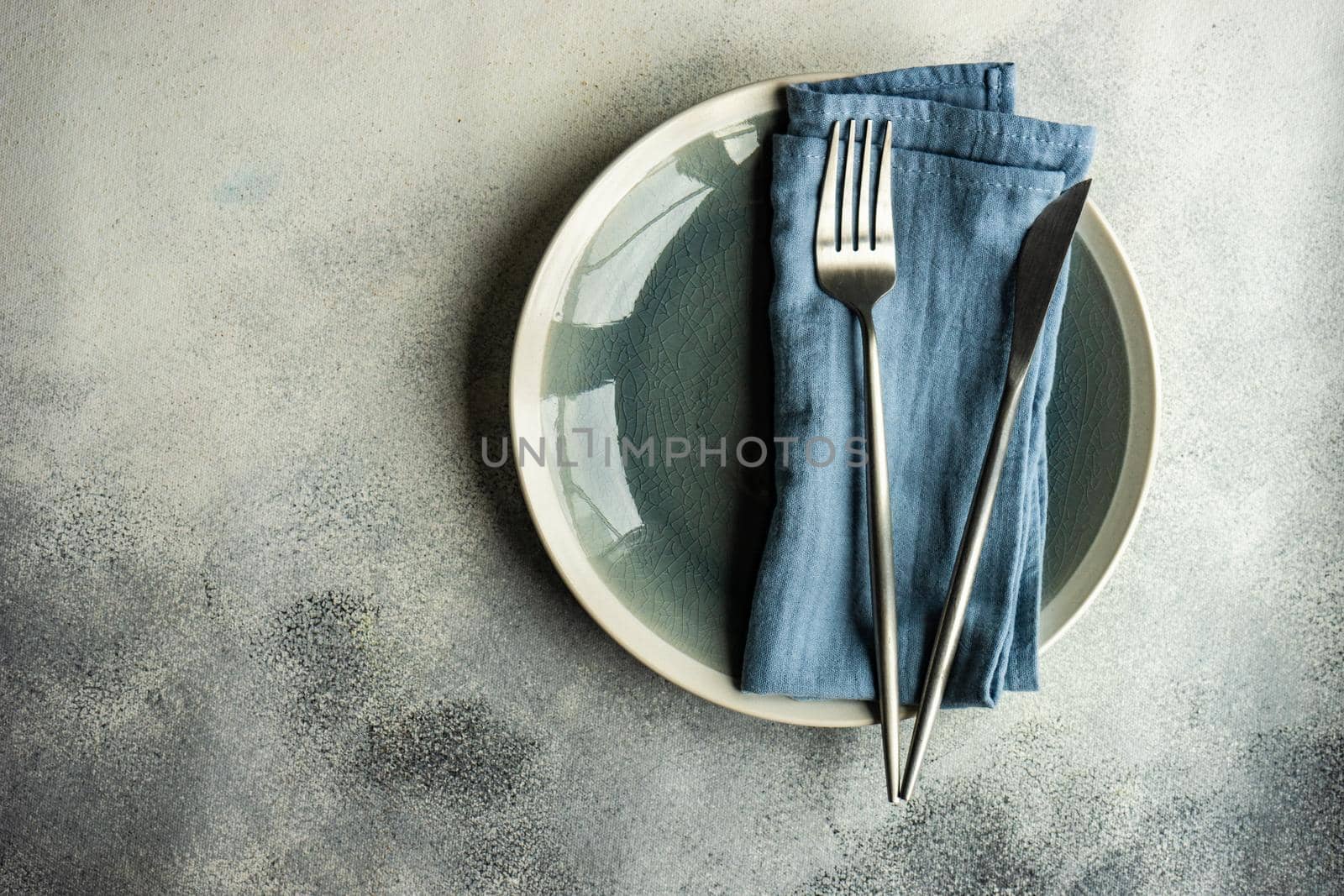 Ceramic plates, same color cutlery with stripped napkin served on grey concrete background