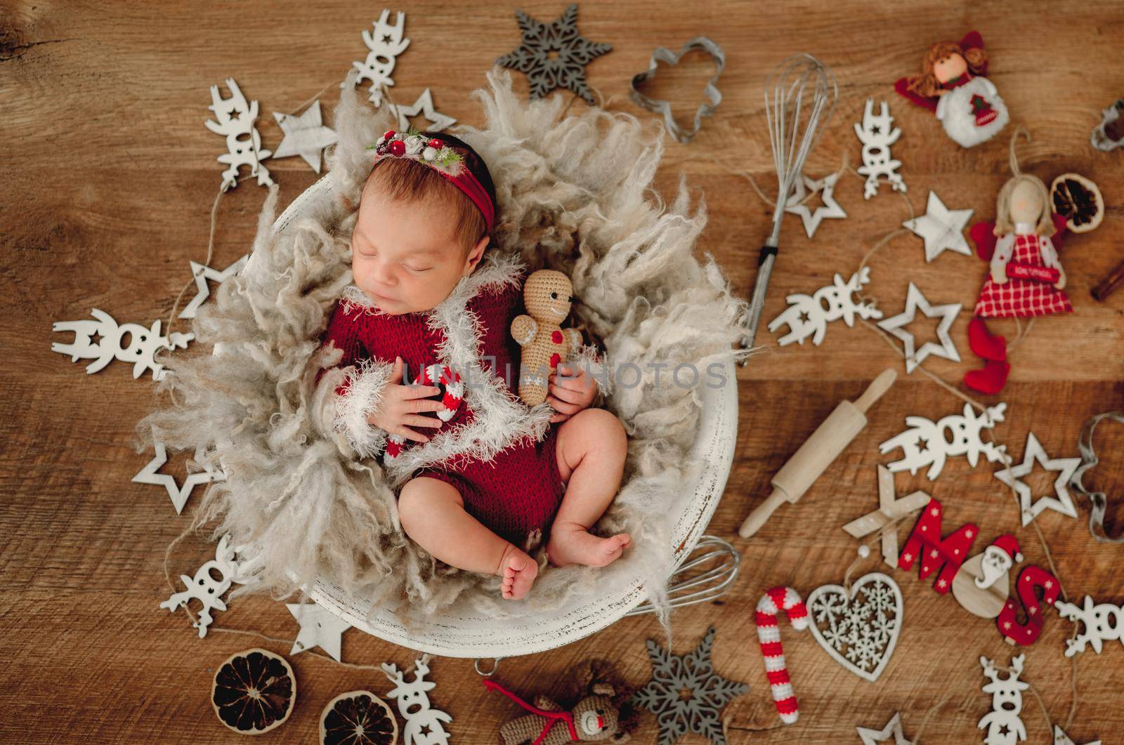 Newborn baby girl sleeping wearing Santa costume and holding knitted ginger man toy lying in basin. Adorable infant child kid napping Christmas portrait