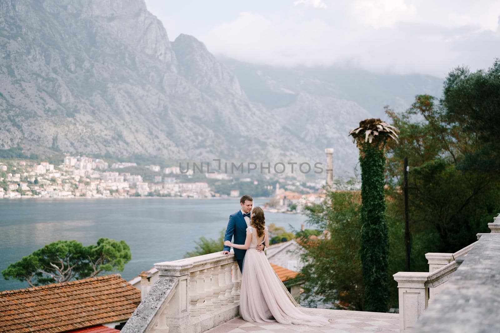 Bride hugs groom on the stone terrace against the backdrop of the bay. High quality photo