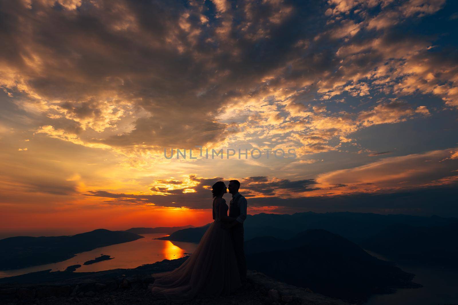 Groom and bride stand on the mountain against the background of sunset by Nadtochiy