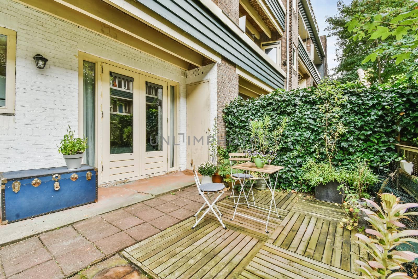 Green backyard of a house with wooden table and chairs and blue chest