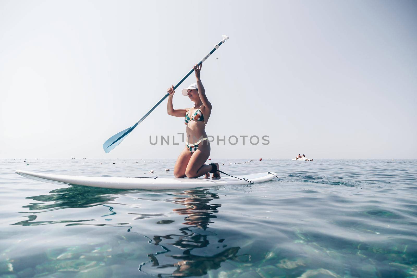 young woman in swimsuits doing yoga on sup board in calm sea, early morning. Balanced pose - concept of healthy life and natural balance between body and mental development
