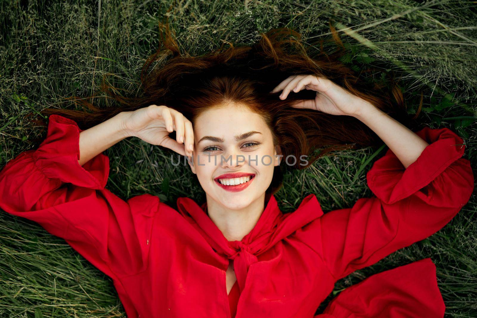 cheerful woman in a red dress lies on the grass top view by Vichizh