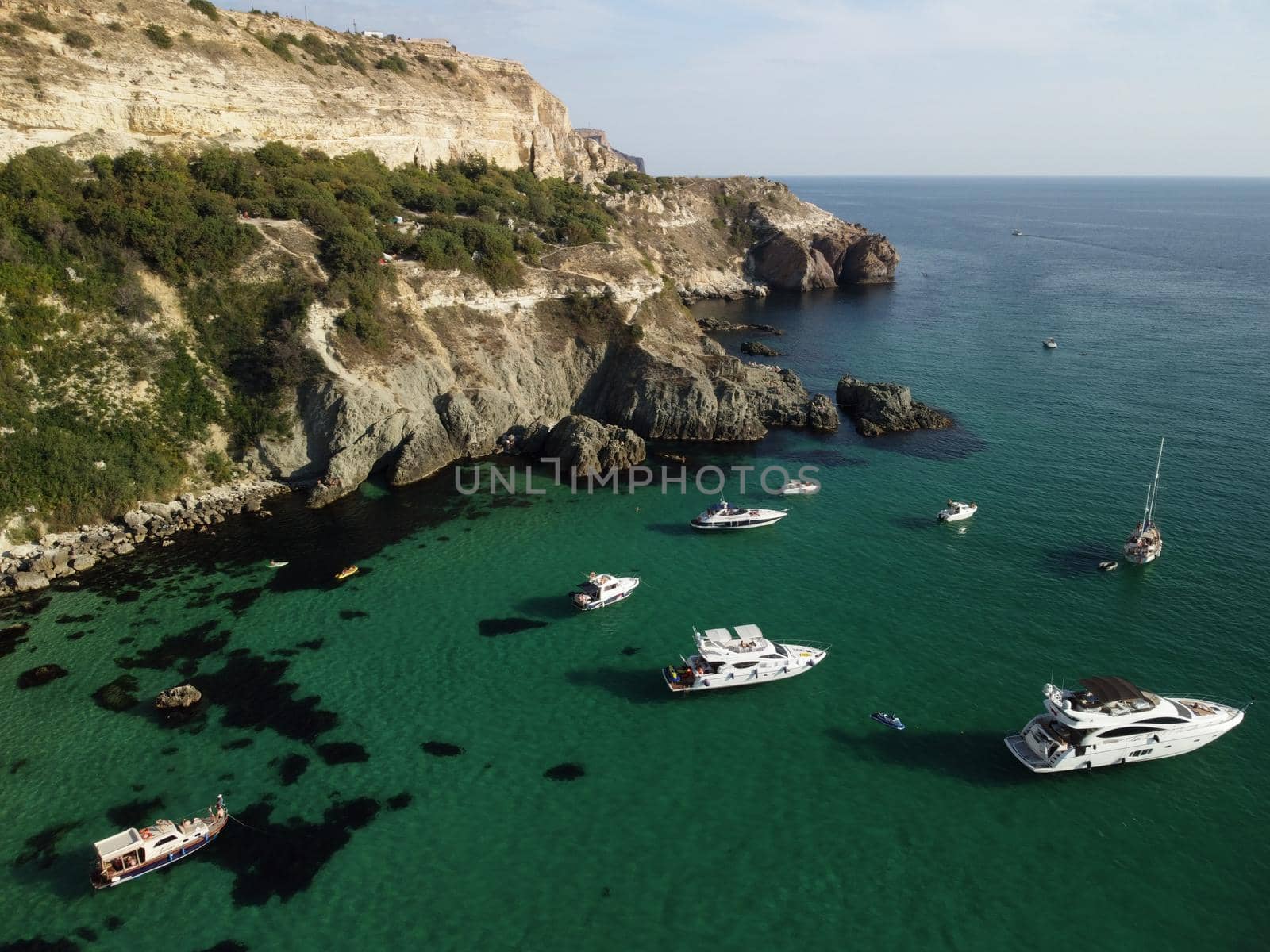 Sea landscape with rocky coastline on sunset time with cloudy sky. Yachts in the Sea on a background of rocky shores. The concept of perfect place for summer travel and rest.