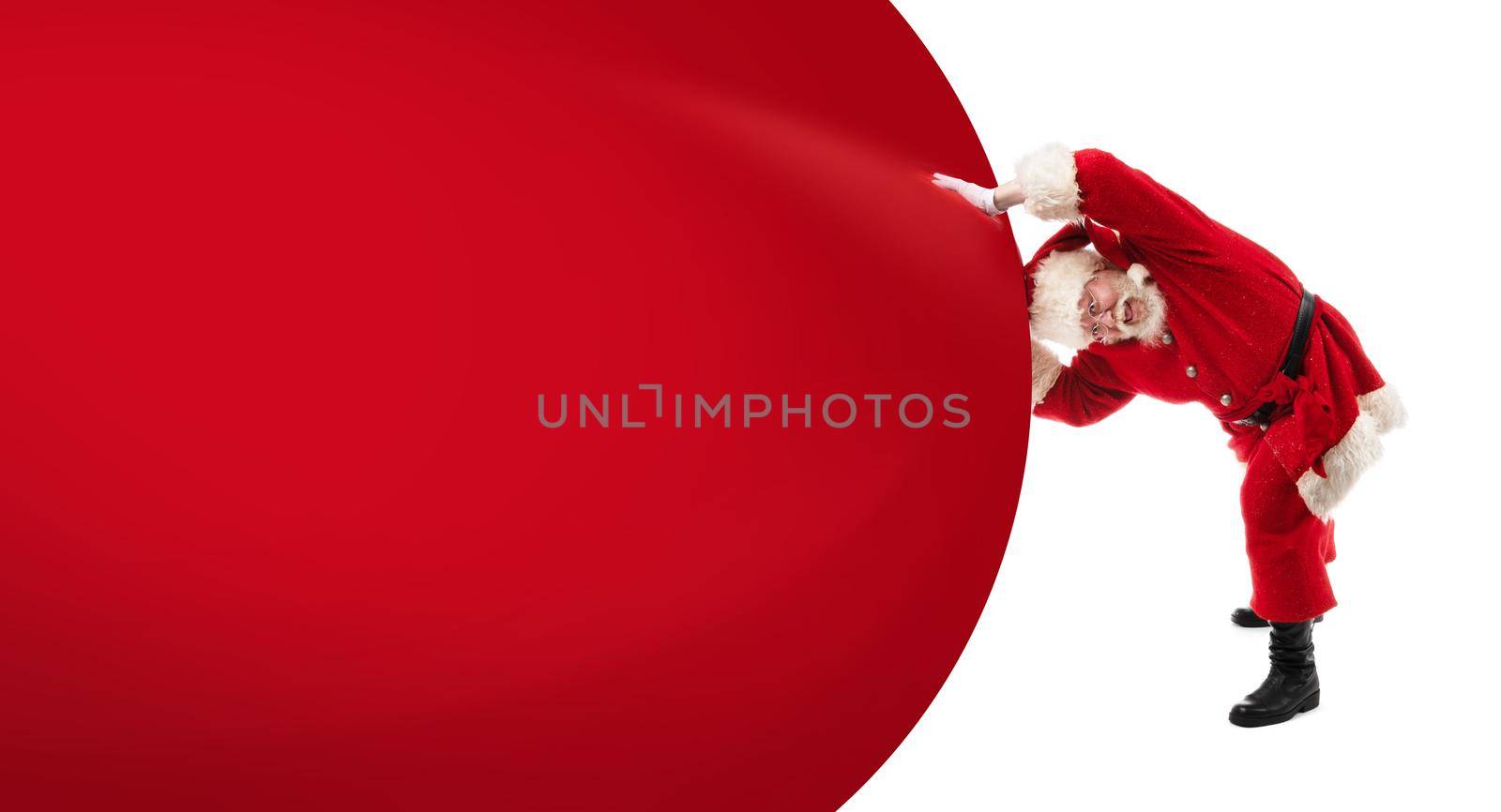 Santa Claus pushing huge bag of gifts isolated on white with copy space for text, big red banner background