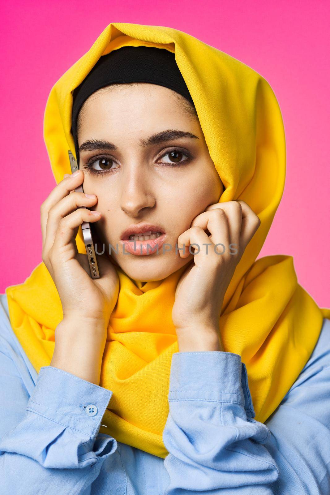 muslim woman in yellow hijab talking on the phone technology pink background. High quality photo