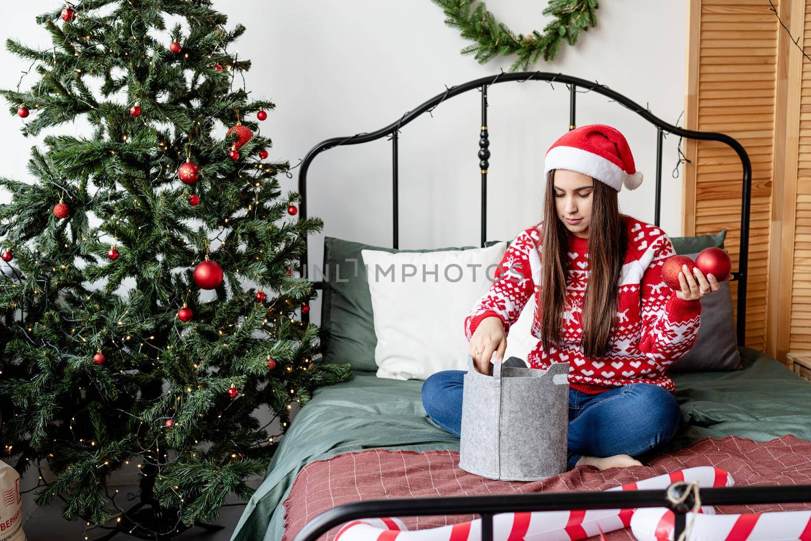 Young woman in red sweater and santa hat sitting on the bed celebrating christmas by Desperada