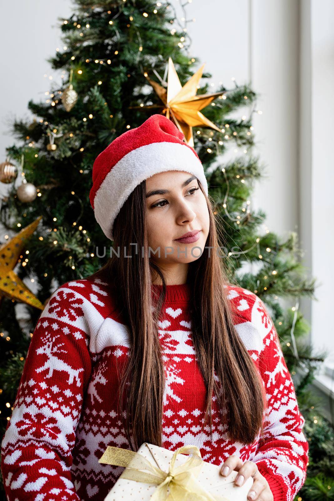 Packaging holiday gifts. Christmas gift wrapping. Young woman in red sweater holding christmas gift