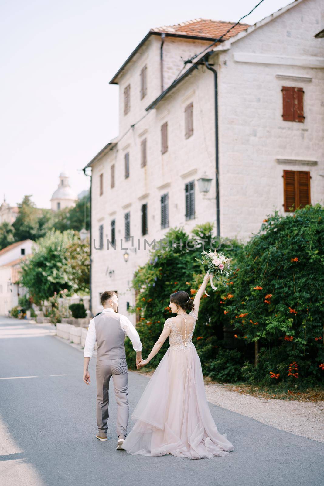 Bride and groom walk down the street past the old building. Back view by Nadtochiy