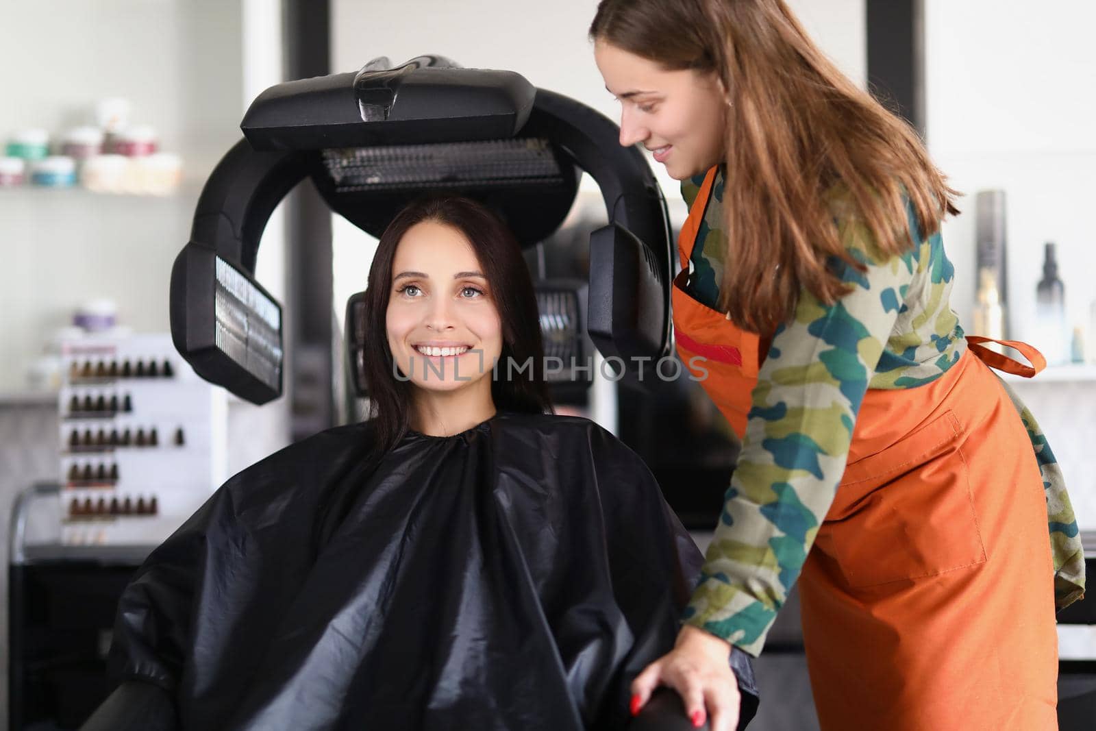 Portrait of young lady under hairdressing machine while looking in mirror. Visit master for beautiful look and good hair quality. Self care, beauty concept