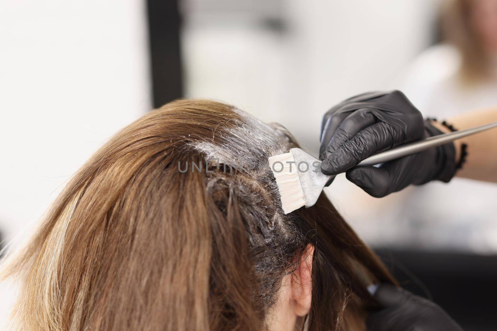 Close-up of hair master apply dye colour on hair with grey brush tool. Female client enjoying beauty procedure. Wellness, beauty salon, self care concept