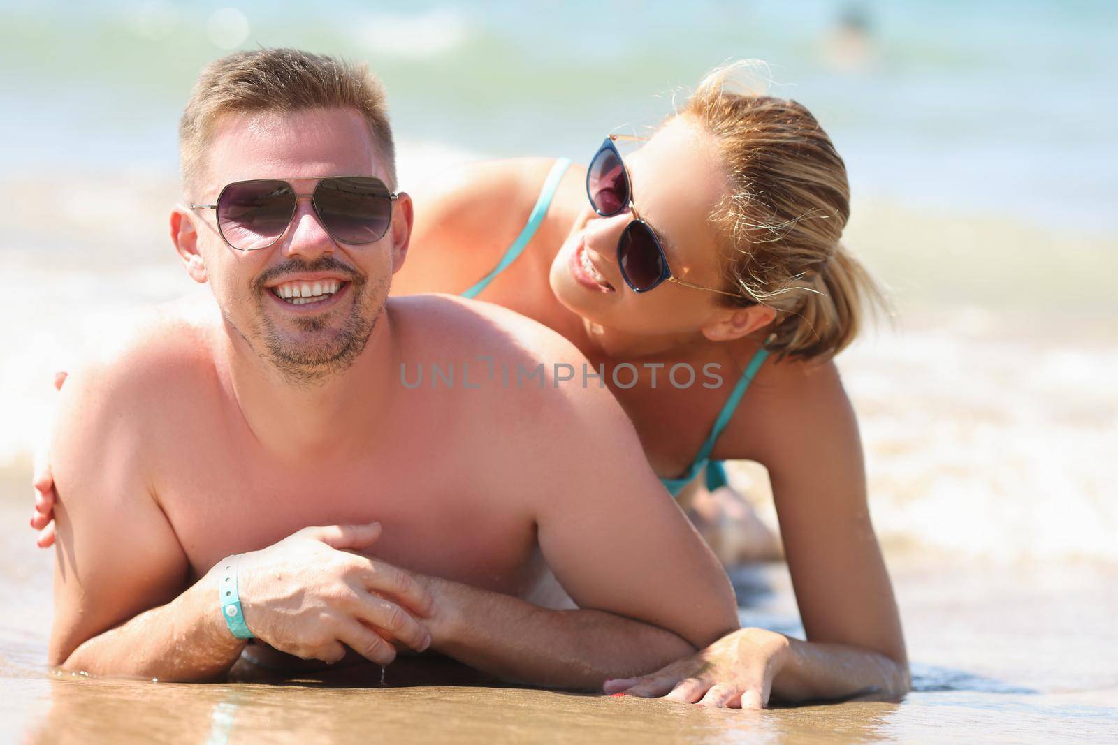 Portrait of cheerful couple resting together on beach laying on coastline and posing. Middle aged man and pretty woman in sunglasses. Beach, summer concept