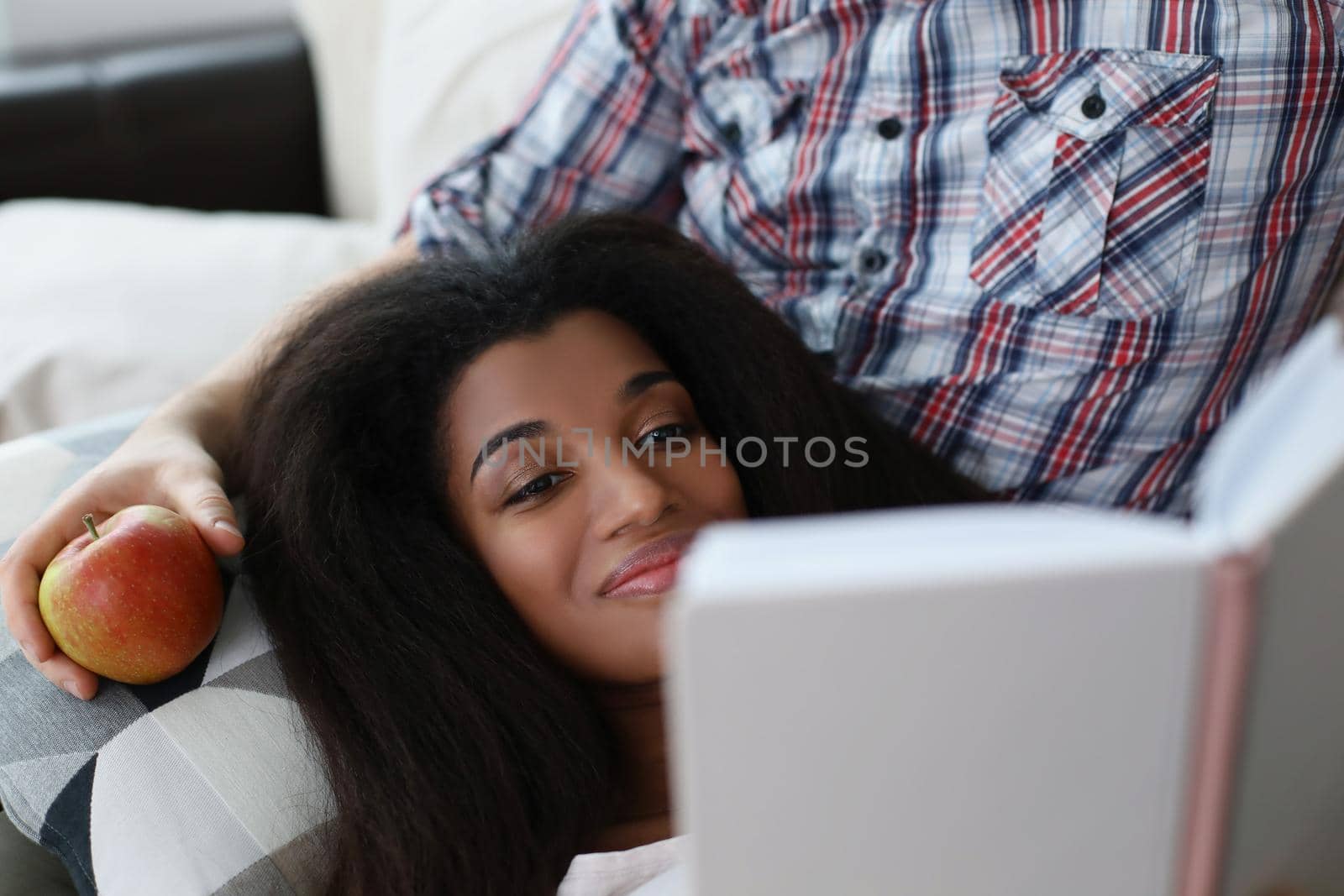 Portrait of latino american young woman reading interesting book laying on fathers lap. Smiling female get new knowledge, spare time at home. Hobby concept