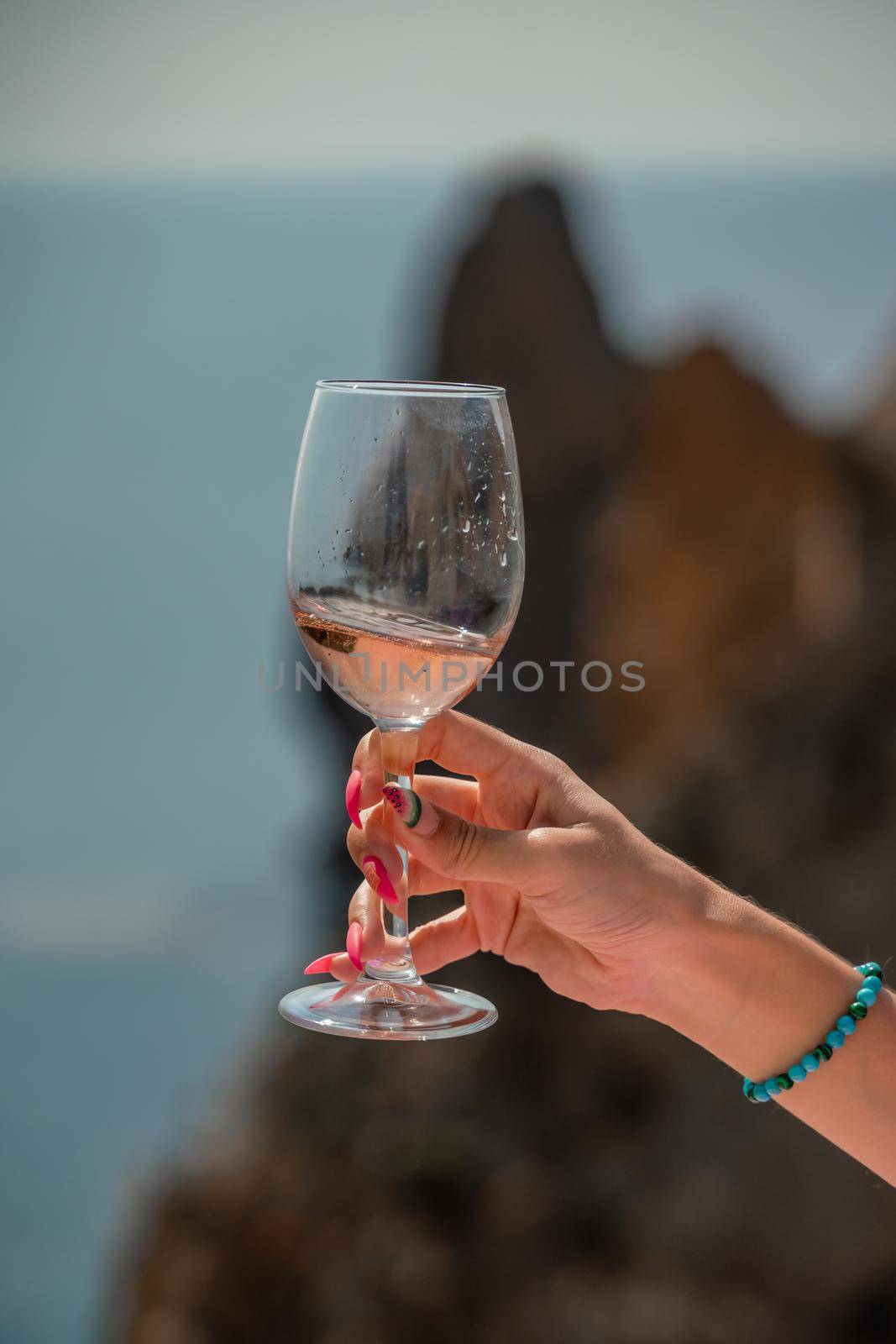 A female hand holds a glass of wine against the background of the sea and mountains. by Matiunina