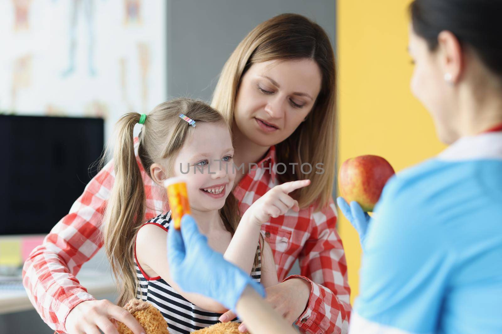 Portrait of happy little girl choose apple instead of bottle of medications. Medical worker in protective gloves and uniform. Pediatrician, clinic concept