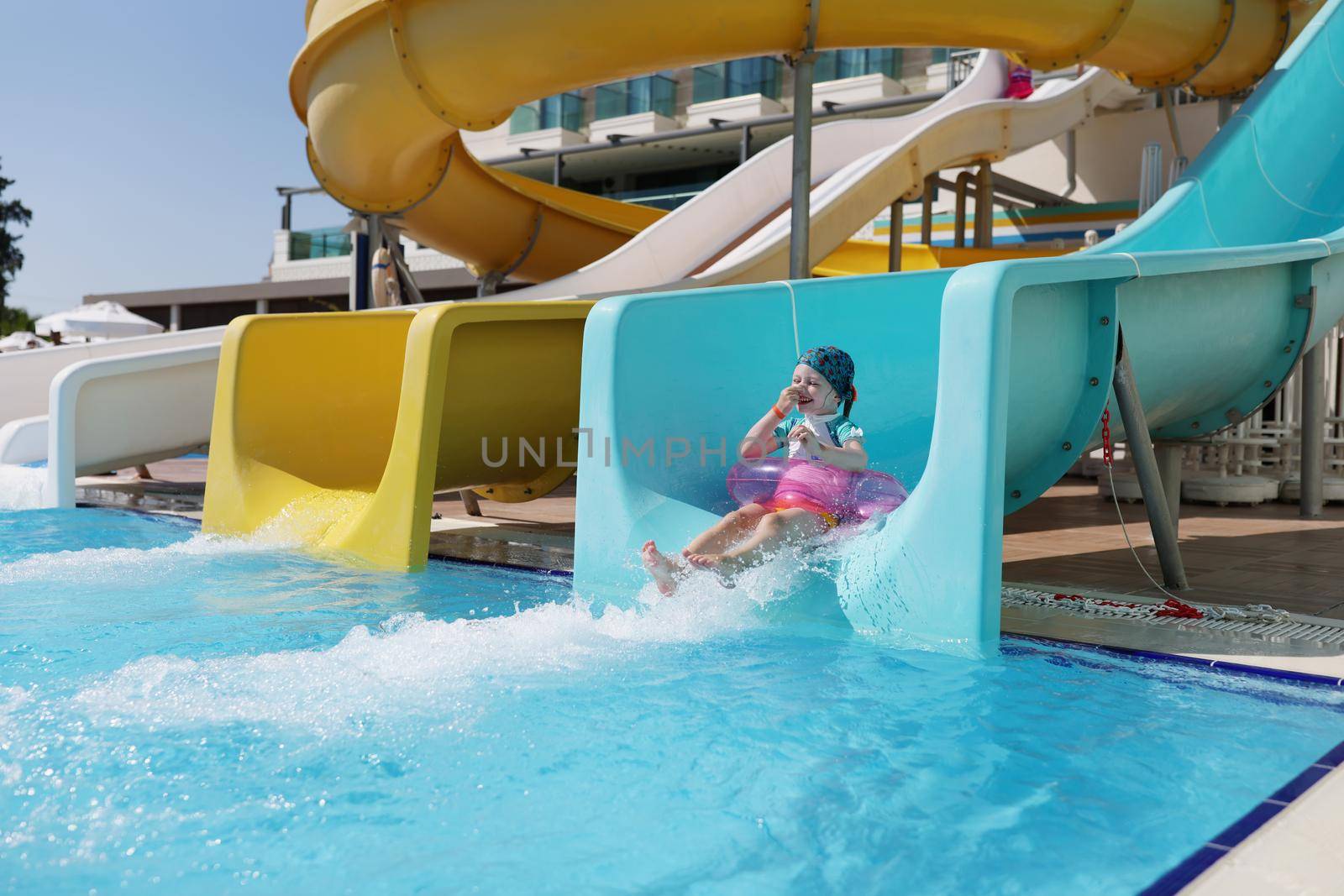 Happy little girl kid slide down hill on pink air mattress in water park by kuprevich