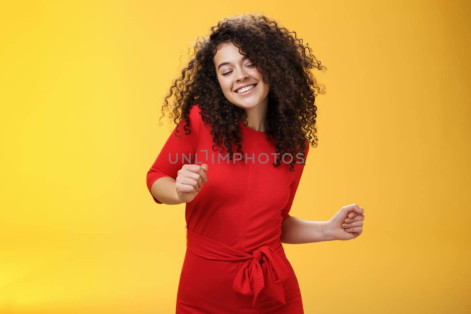 Carefree woman dancing on dance floor with close eyes and smile enjoying life feeling happy and joyful close eyes and making tender expression as moving to rhythm of music over yellow background by Benzoix