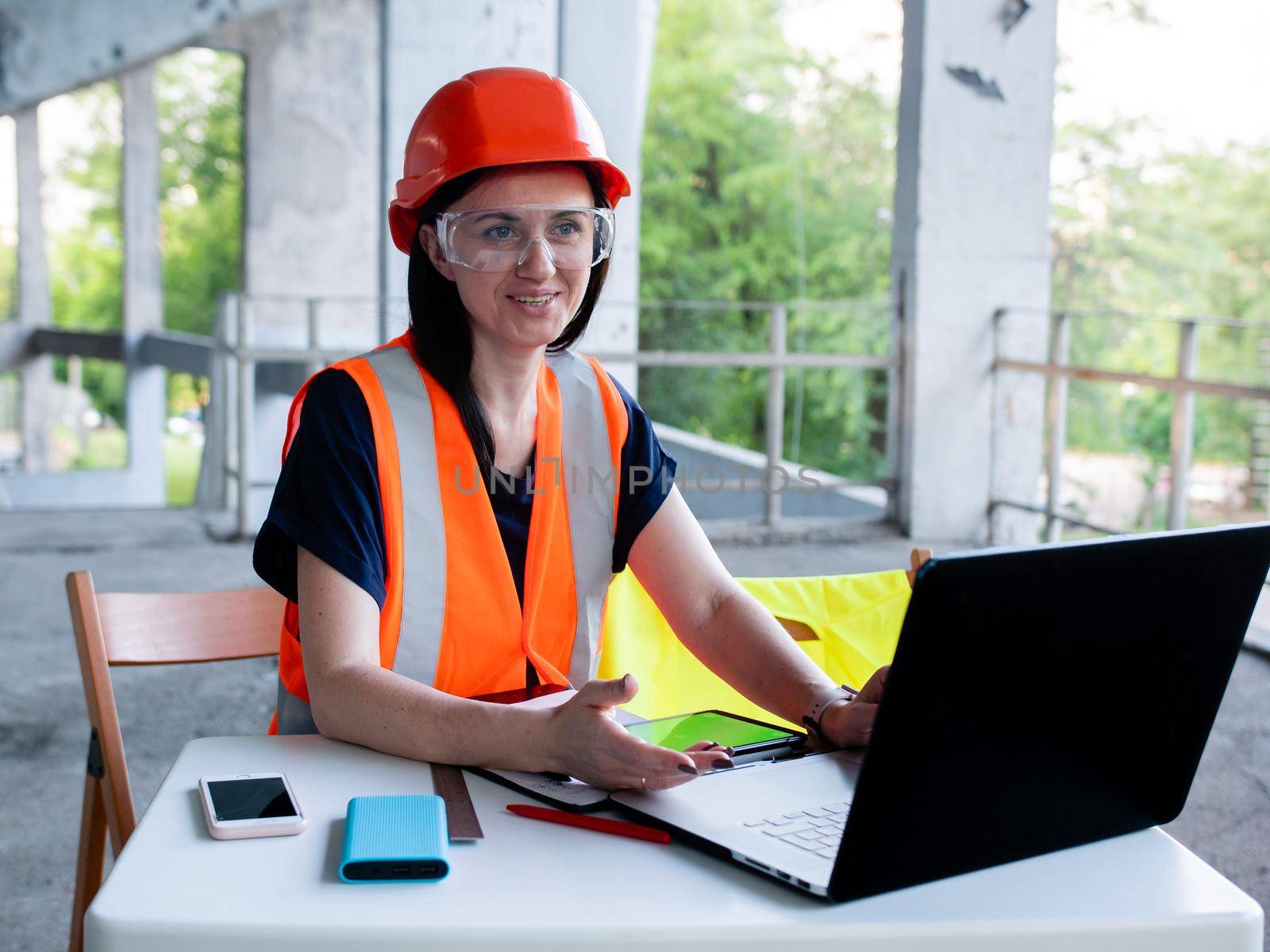 Girl foreman with laptop at construction site. A female engineer works on a computer on the background of a building under construction.