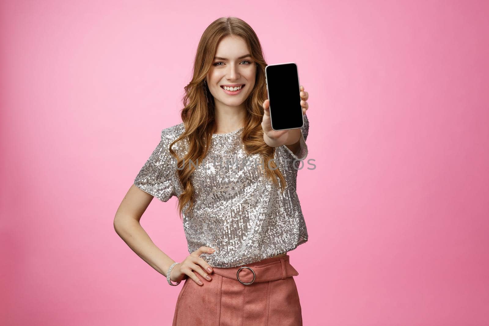 Studio shot confident charismatic young glamour woman introduce awesome smartphone app showing mobile phone display smiling self-assured recommend follow blogger page, standing pink background.