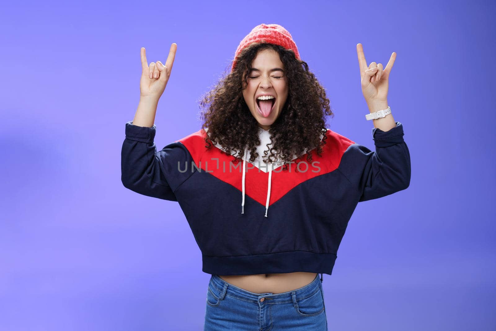 Waist-up shot of rebellious and carefree woman having fun feeling excited and awesome at party close eyes sticking out tongue and showing rock-n-roll signs, wearing beanie and warm clothes.