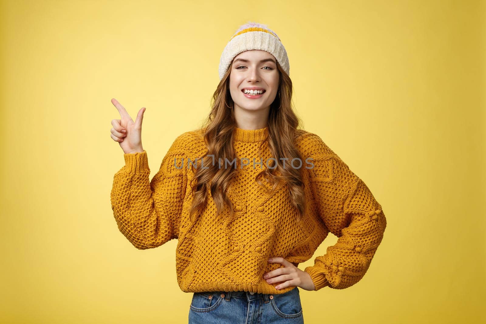 Confident fashionable 20s girl proudly smiling hold hand waist self-assured pointing upper left corner showing perfect copy space top advertisement, promoting product grinning delighted.