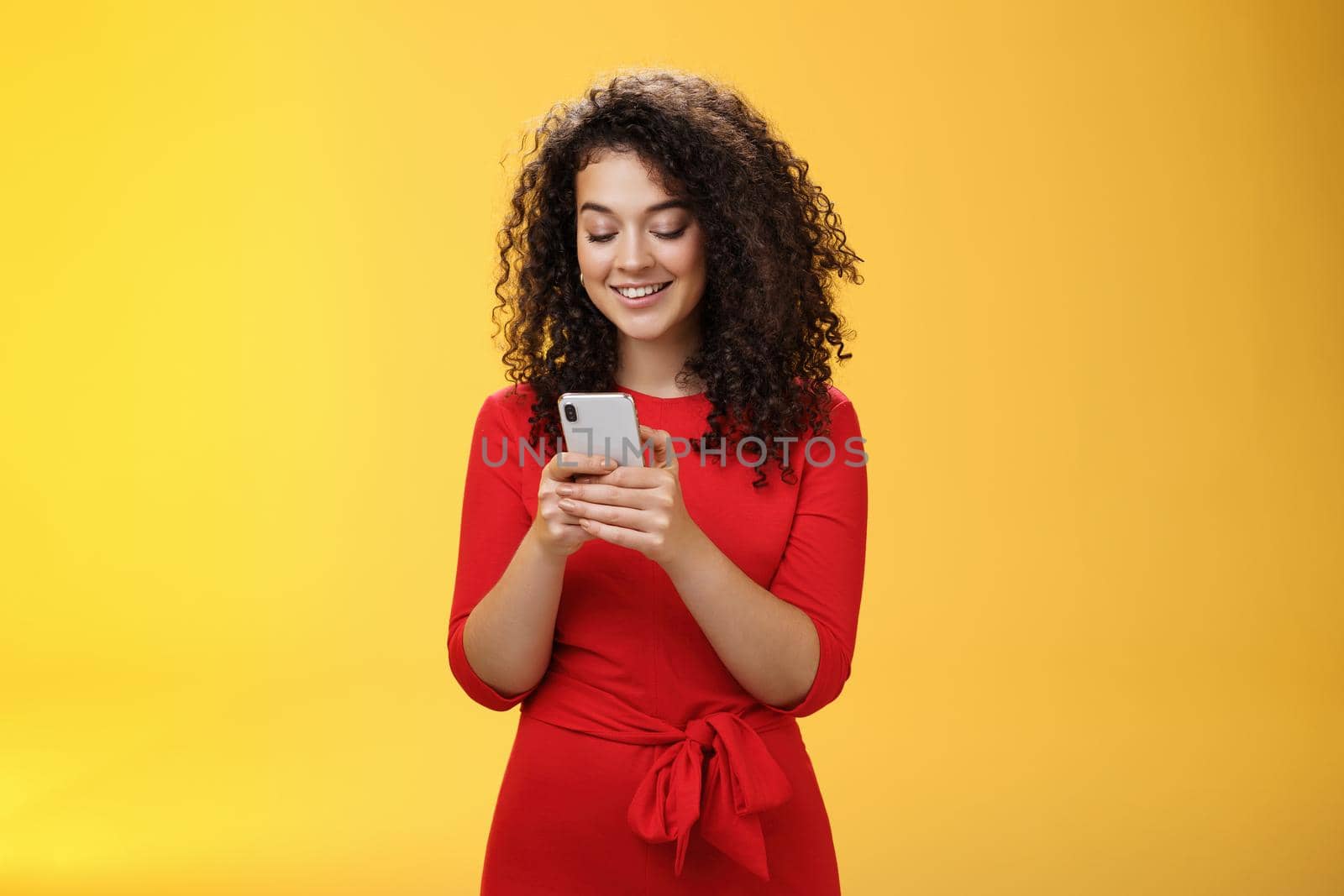 Gil sending message spread news across social network having party inviting friends via smartphone holding mobile phone in hands smiling broadly at device screen as posing over yellow background by Benzoix