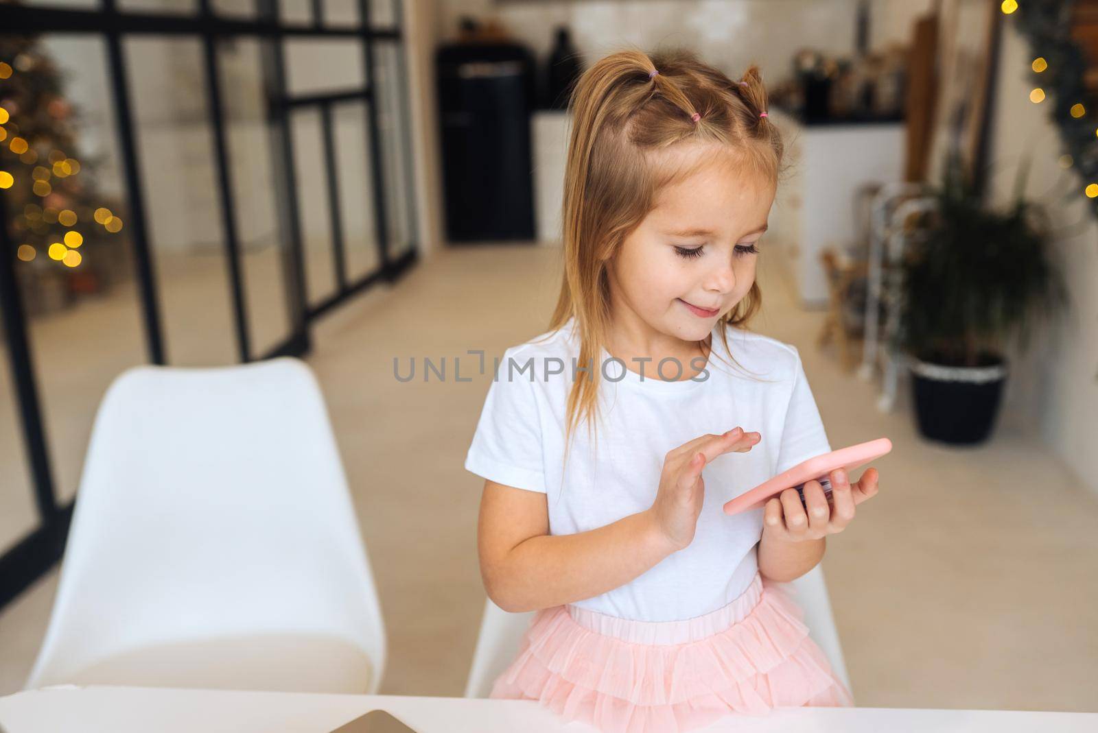 Little kid sit at desk with laptop hold mobile phone at home